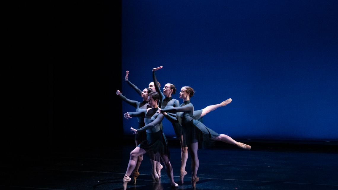 group of dancers on stage, all in dark gray.