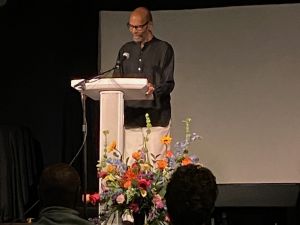 Standing behind a pew, Professor Clay Taliaferro speaks at an event in his honor