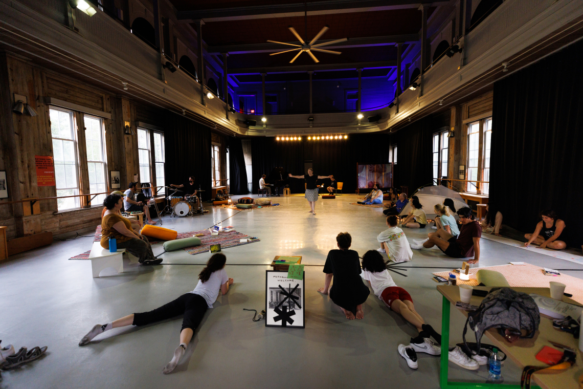 Dance instructor standing in the middle of the room with students sitting around the room